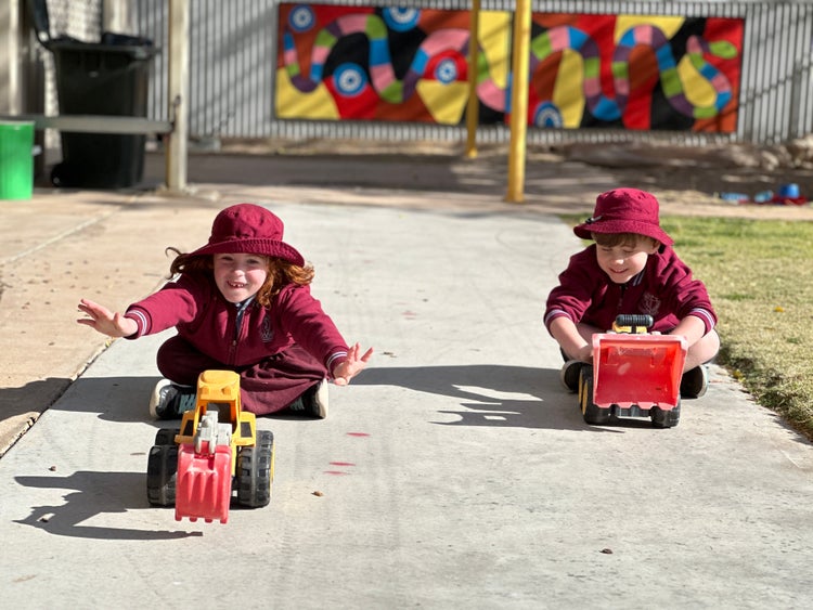 Boy and girl racing toy trucks on concrete path.