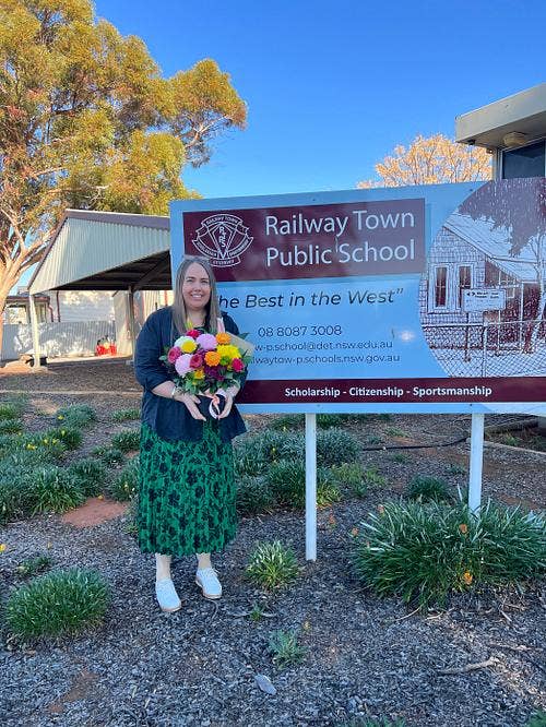 teacher holding flowers in front of school sign